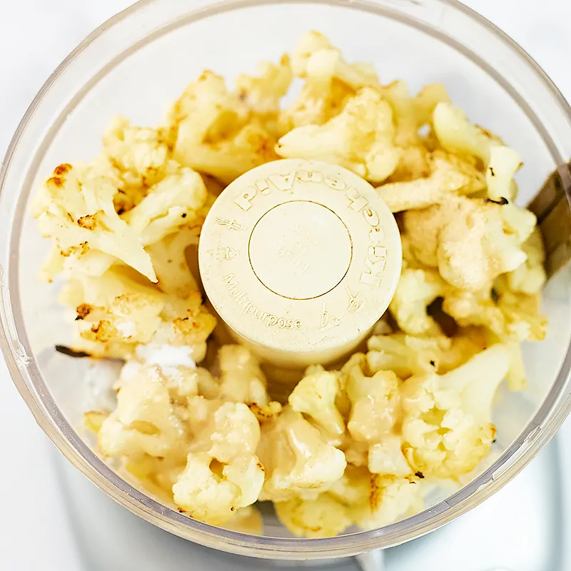 Food processor filled with ingredients to make creamy roasted cauliflower hummus