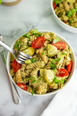 Silver fork in a bowl of artichoke pesto pasta.