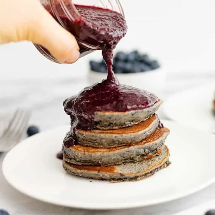 stack of 4 pancakes being with blueberry syrup poured over top