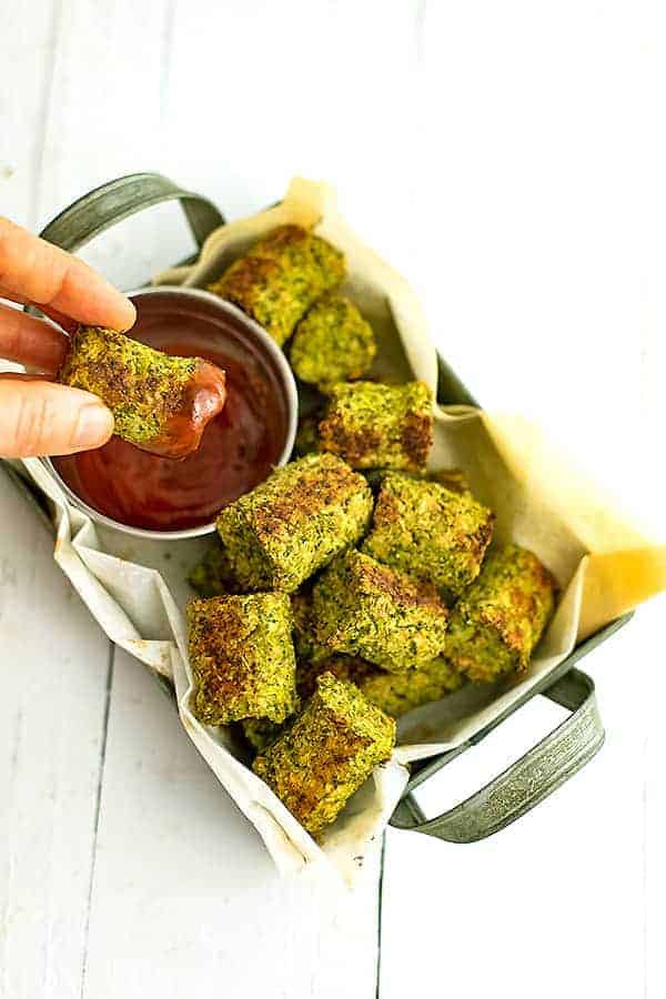 Broccoli tots in rectangular tray with a tot being dipped into ketchup