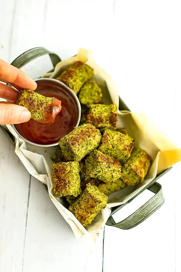Broccoli tots in rectangular tray with a tot being dipped into ketchup