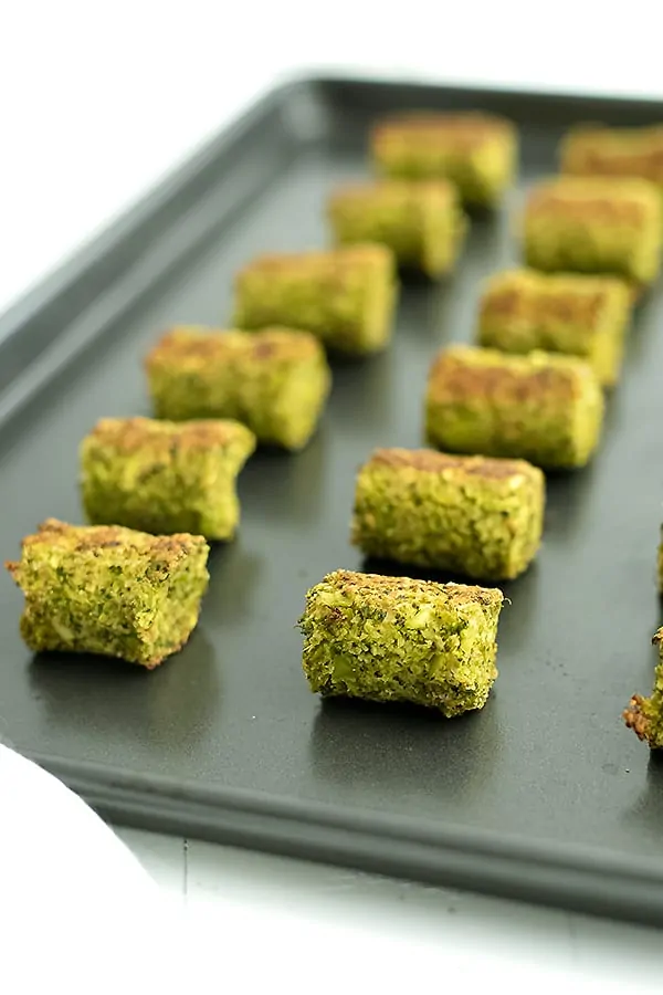 Rimmed baking sheet full of broccoli tots lined up in rows. 
