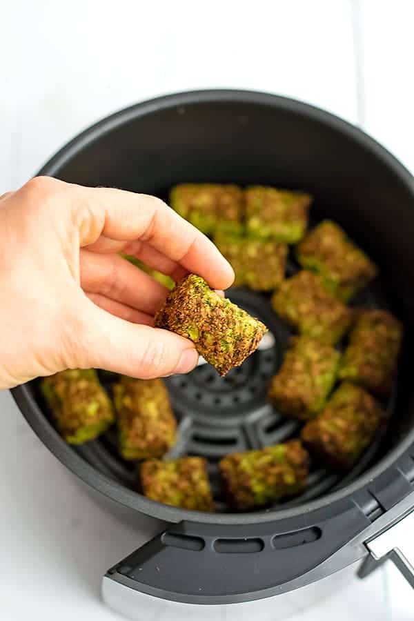 AIr fryer of broccoli tots with hand holding one tot.