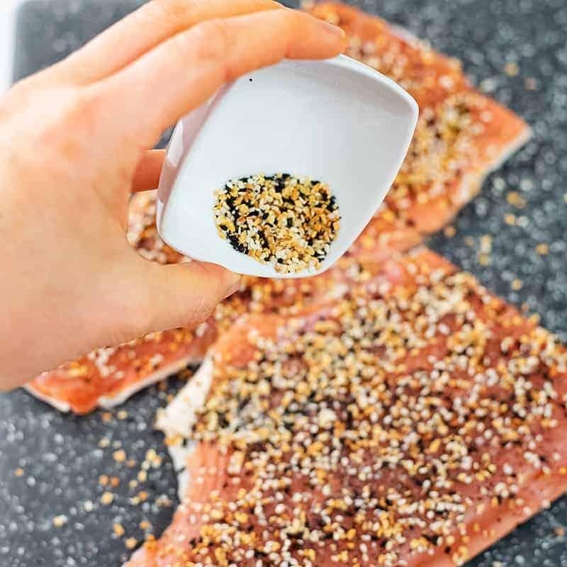 Hand sprinkling everything bagel seasoning over salmon