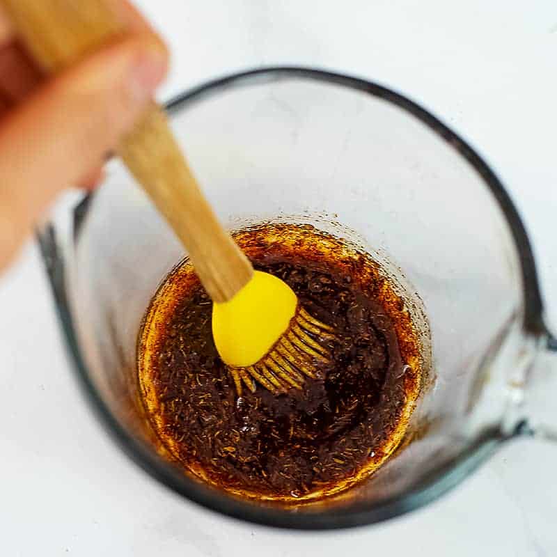 Silicone brush mixing olive oil and spices in glass jar