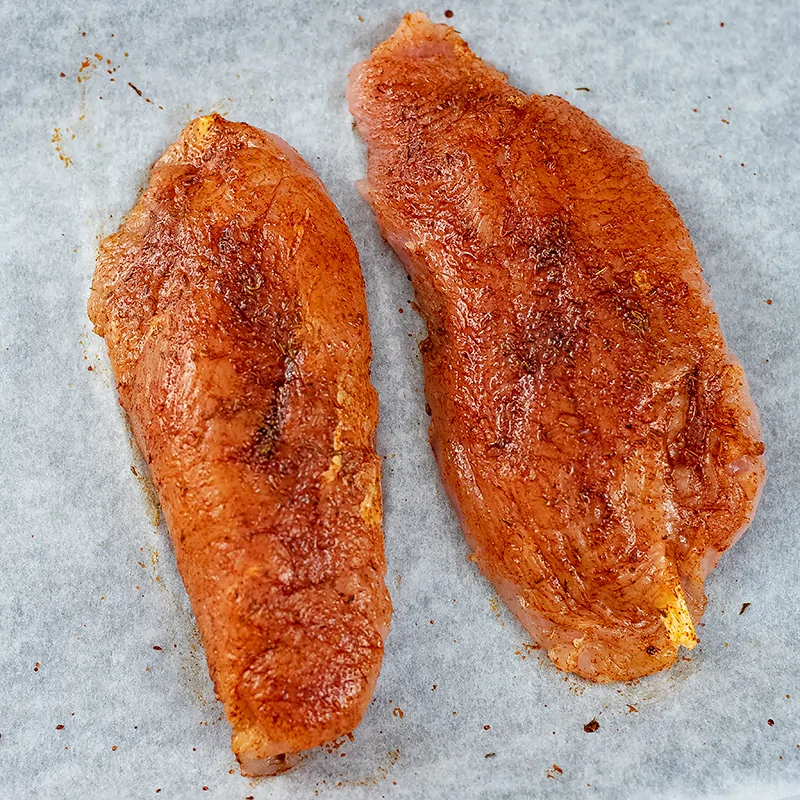 Two chicken breast covered in spice rub before baking