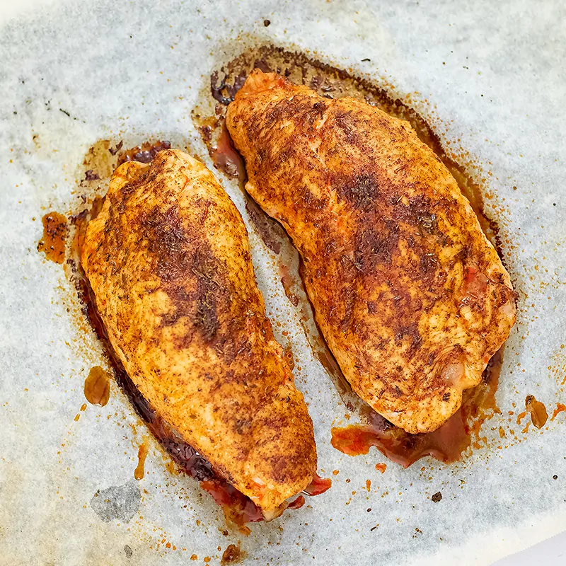 2 baked chicken breast on parchment paper before slicing