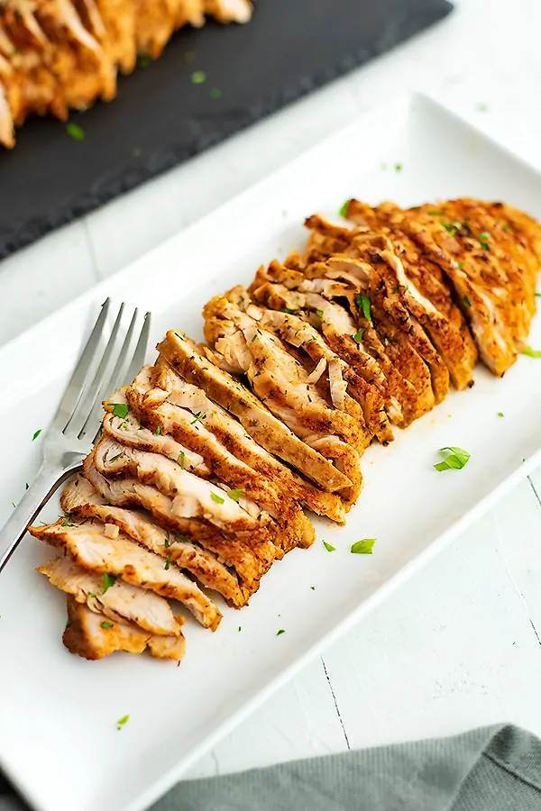 Thinly sliced oven baked chicken breast on white plate with fork