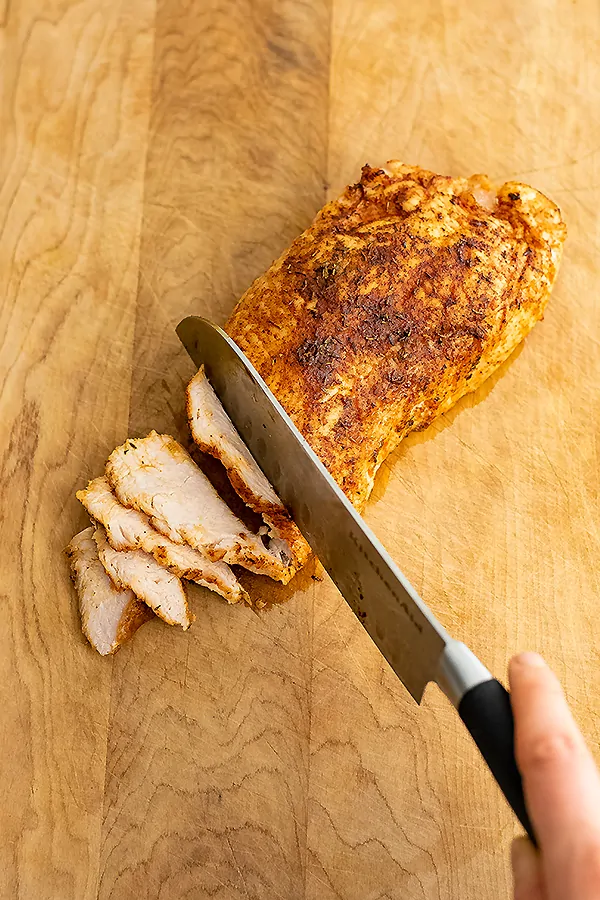 Chicken breast on a cutting board being cut with knife