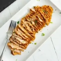Thinly sliced oven baked chicken breast on white plate with fork