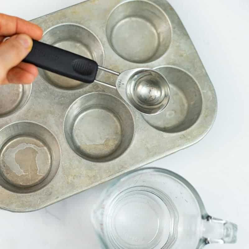 Silver muffin tin with tablespoon of water being added to the tin