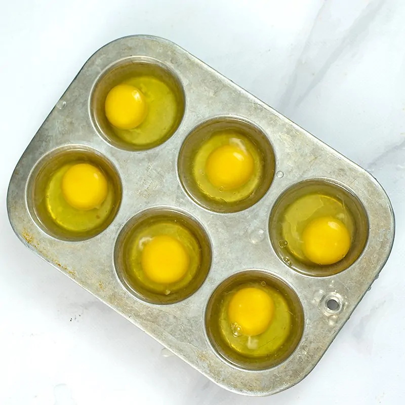 Raw eggs cracked into the muffin tin