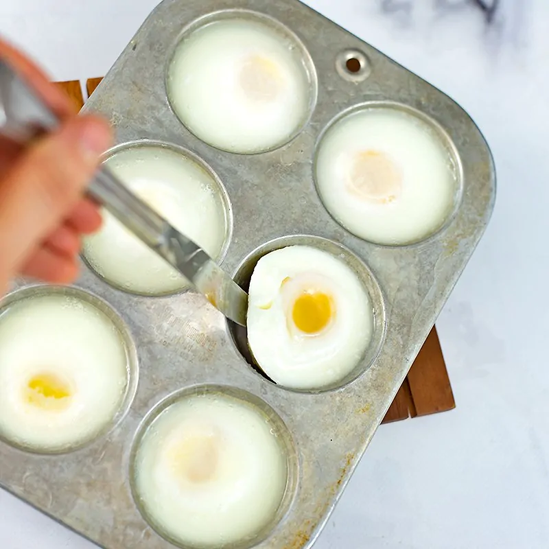 Cooked eggs being removed from the muffin tin with knife