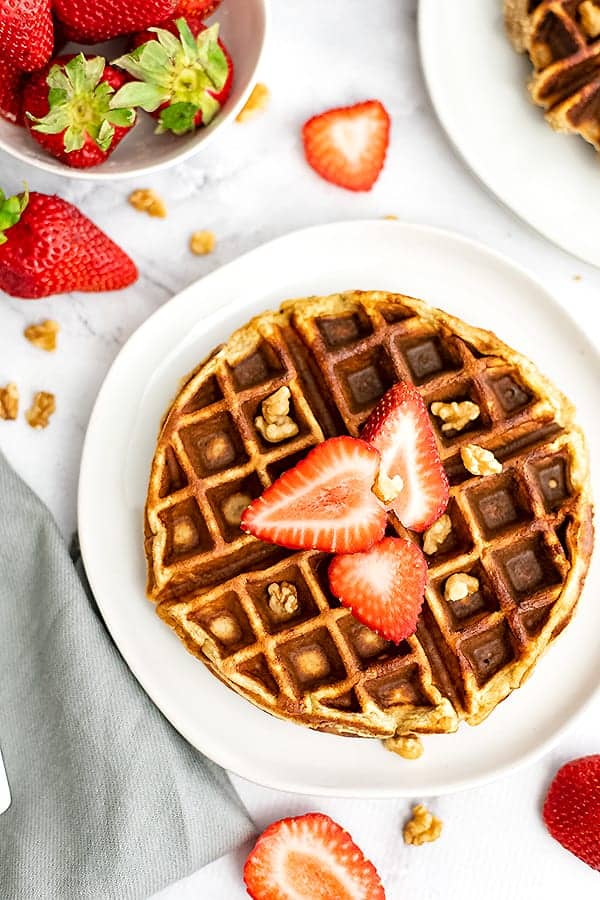 Protein waffles with sliced waffles and chopped walnuts. Strawberries in background
