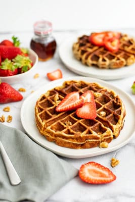 Two protein waffles with strawberries on top with syrup in the background