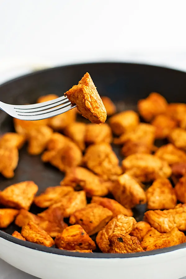 Piece of chicken on a fork over a skillet of chicken