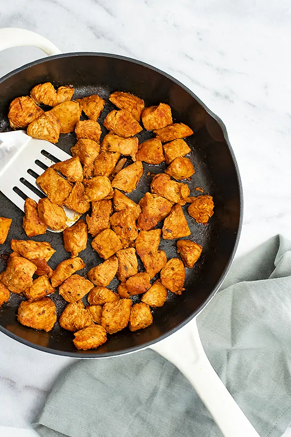 Cast iron skillet filled with taco chicken and silver spatula