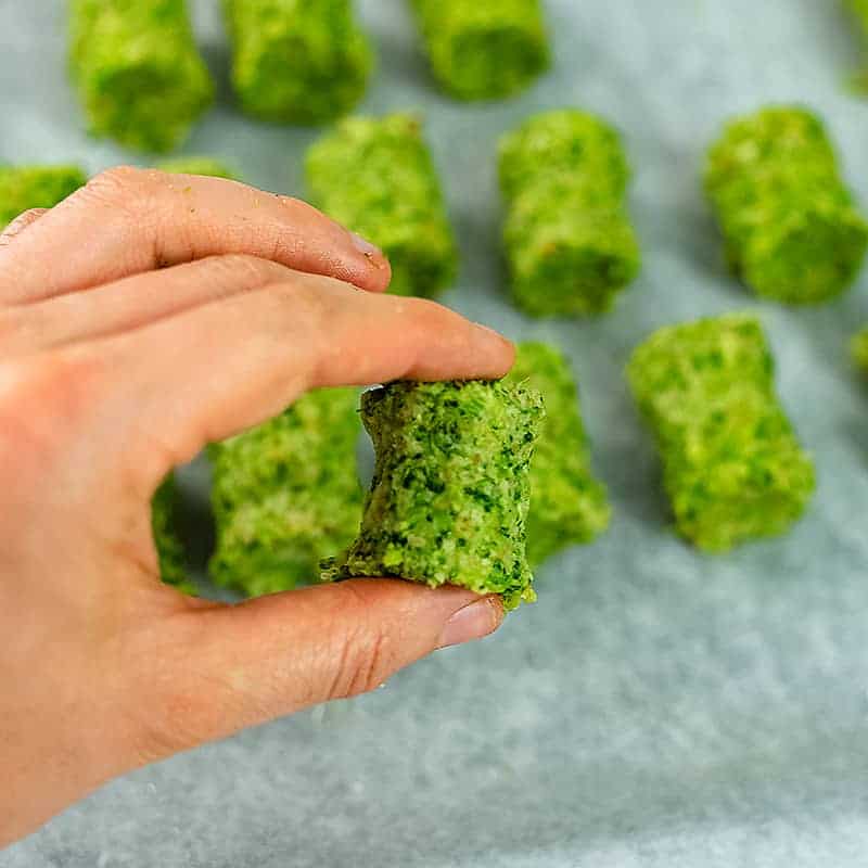 Hand holding a single broccoli tot before baking.