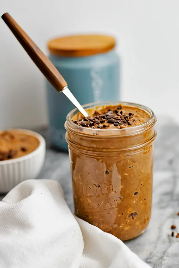 Mason jar filled with mocha overnight oats and wooden spoon