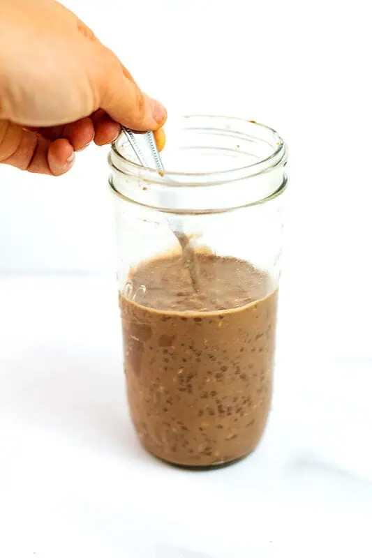 Hand stirring a spoon in jar of overnight oats with coffee.