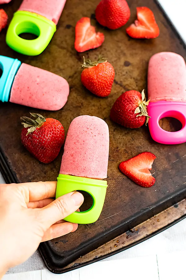 Hand holding popsicle over a tray of strawberries and popsicles