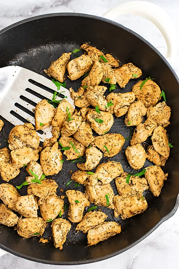 Cast iron skillet with Italian Chicken and a silver spatula