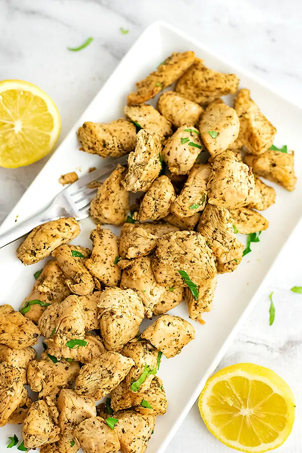 White plate filled with Italian Chicken surrounded by sliced lemons