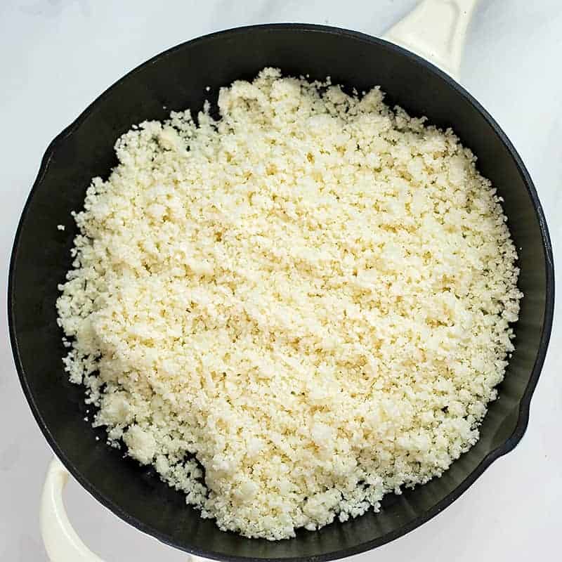 Cast iron skillet filled with riced cauliflower.
