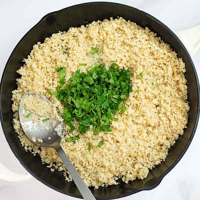 Cooked cauliflower rice with cilantro on top in a cast iron skillet