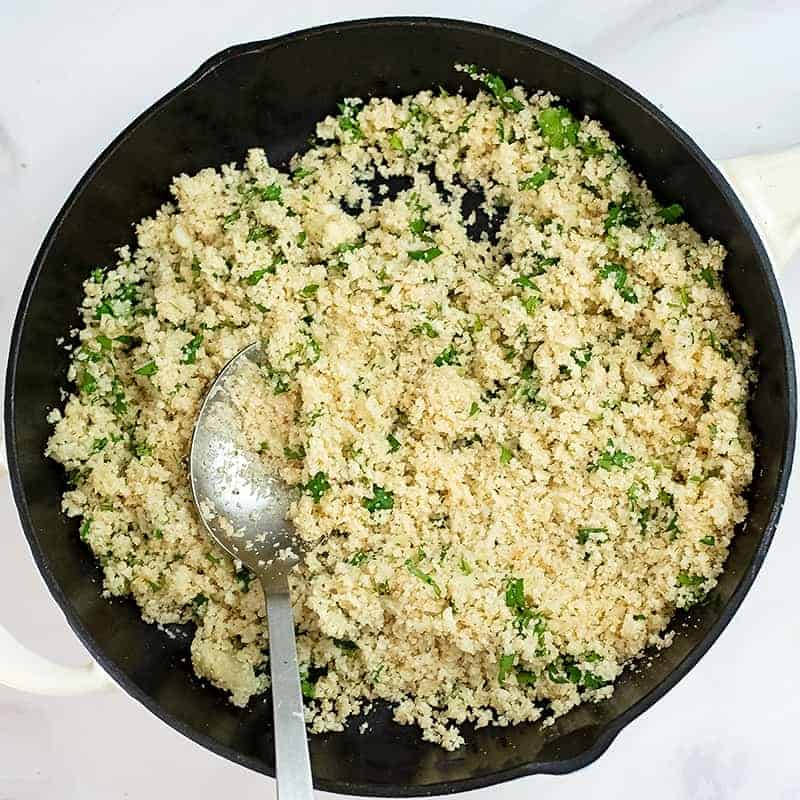 Cast iron skillet filled with cilantro lime cauliflower rice and silver serving spoon
