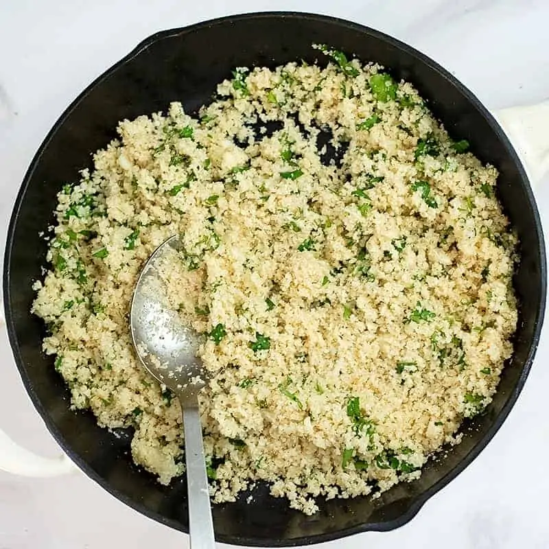 Cast iron skillet filled with cilantro lime cauliflower rice and silver serving spoon