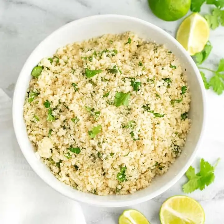 Large white bowl filled with cilantro lime cauliflower rice with limes around the bowl.
