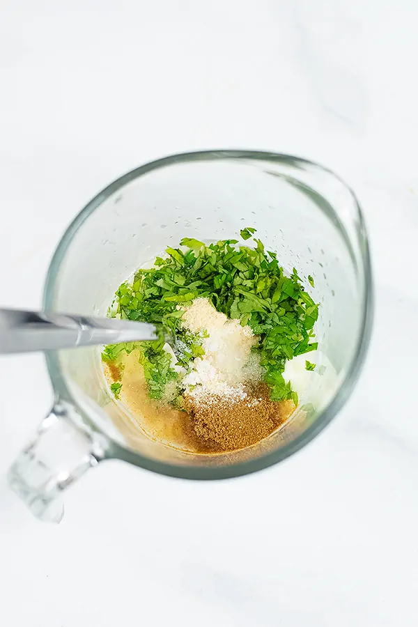 Glass measuring cup filled with ingredients for cilantro lime yogurt sauce
