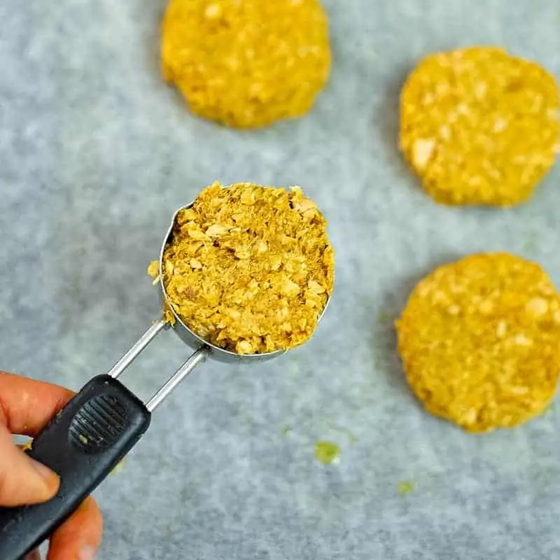 Hand holding measuring cup filled with curry salmon patty mixture