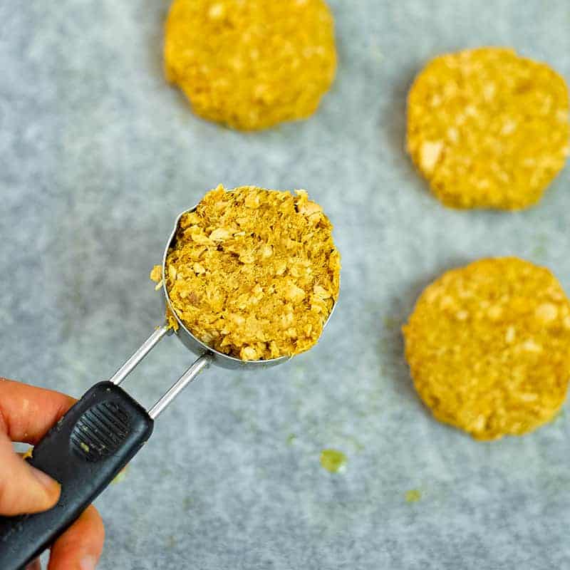 Hand holding measuring cup filled with curry salmon patty mixture