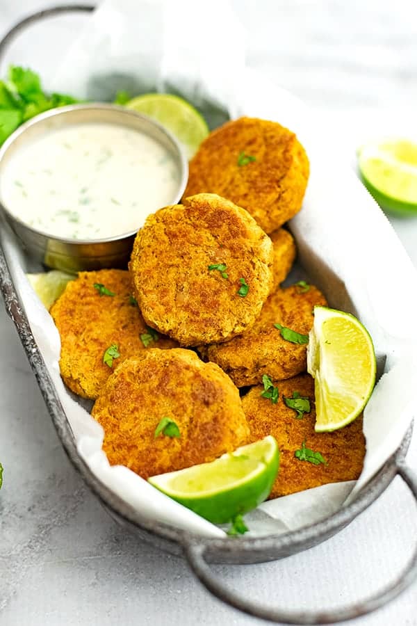 Curry salmon cakes with cilantro lime yogurt in basket with sliced limes