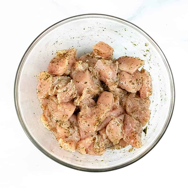 Large bowl filled with cubed chicken coated in Italian seasoning.
