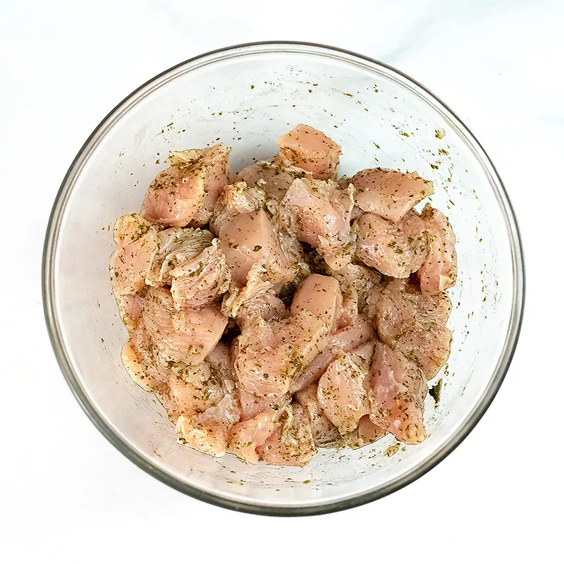 Large bowl filled with cubed chicken coated in Italian seasoning.