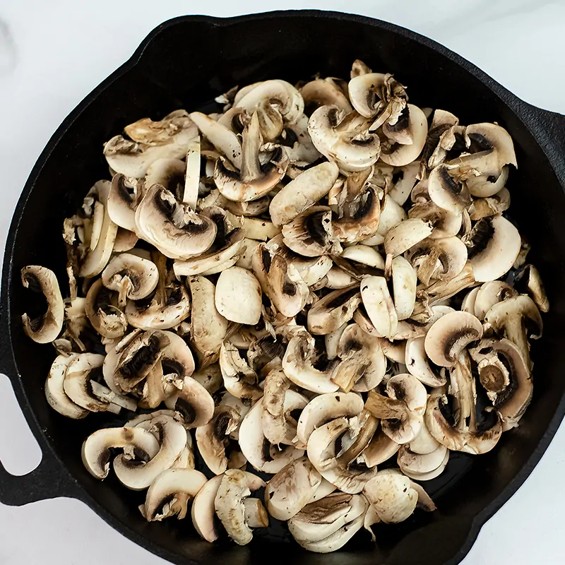 Sliced mushrooms in a cast iron skillet before cooking. 