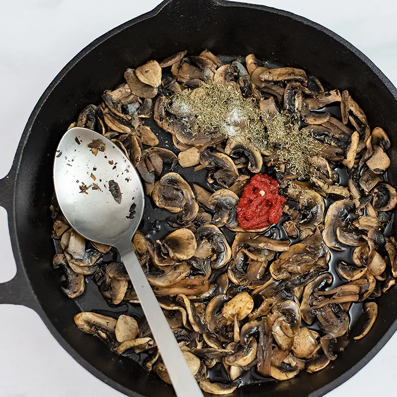 Cooked mushrooms in a skillet with spices, tomato paste on top. 