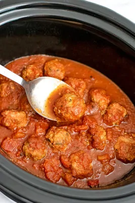 Whole30 Turkey Meatballs in a crockpot, silver serving spoon holding one meatball