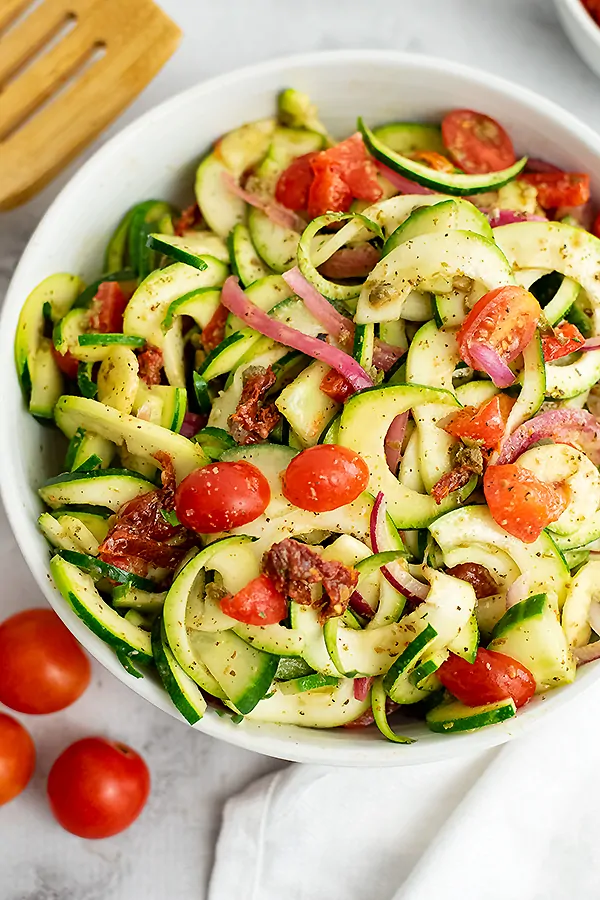 Large bowl filled with zucchini pasta salad with tomatoes in background.
