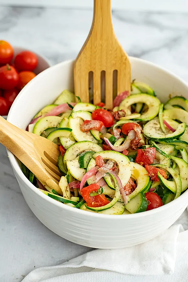Wooden spoons in a bowl of zucchini pasta salad italian dressing