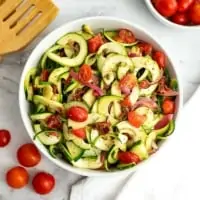 Bowl of zucchini pasta salad with tomatoes and spoon in background