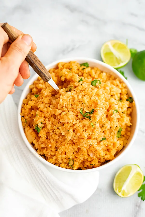 Hand holding spoon with wood handle in a bowl of Tex-Mex cauliflower rice.