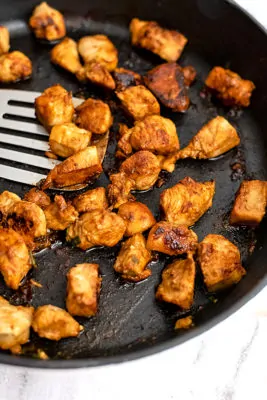 Cast iron skillet filled with asian chicken with silver spatula.