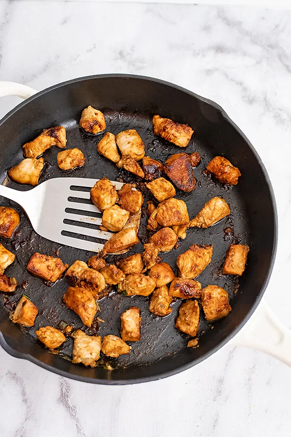 Large cast iron skillet filled with Asian Chicken and a silver spatula.