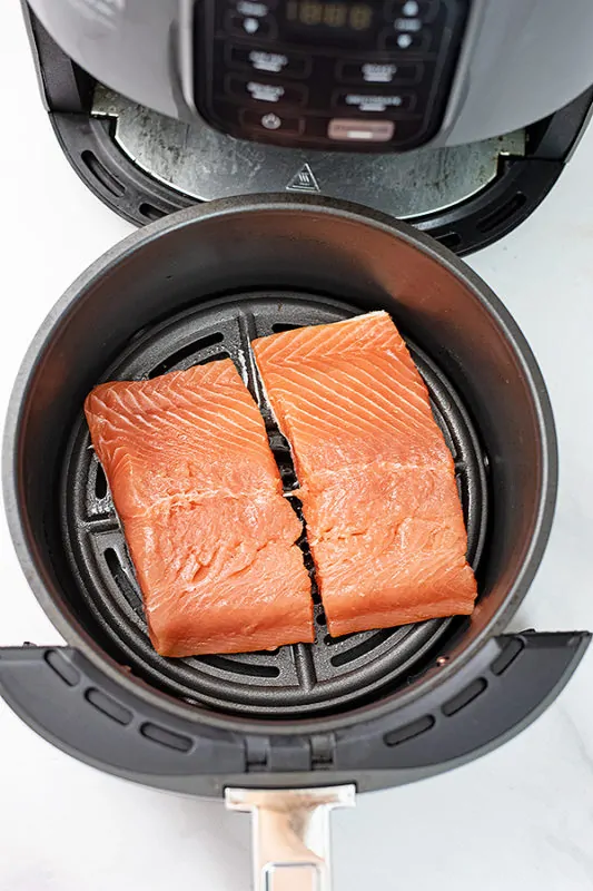 Raw salmon in an air fryer basket.