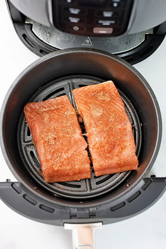 Salmon in the air fryer with seasoning sprinkled on raw salmon.