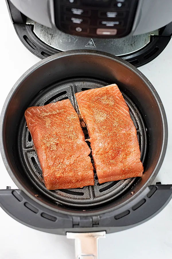 Salmon in the air fryer with seasoning sprinkled on raw salmon.